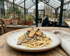 Linguine mit Pilzen, Kräutern und gebratenen Austernpilzen auf einem Holztisch in einem Gewächshausrestaurant.