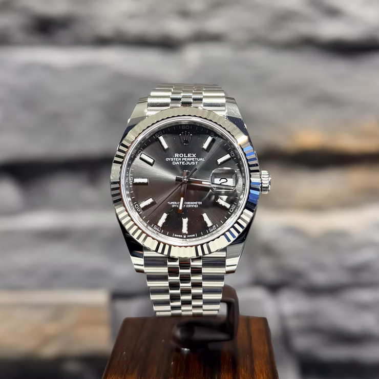 Silberne Rolex Oyster Perpetual Datejust Uhr mit anthrazitfarbenem Zifferblatt und geriffelter Lünette auf Holzständer.