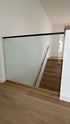 Verglaste Brüstung mit schwarzem Geländer, die zu einer Holztreppe mit Holzhandlauf führt.