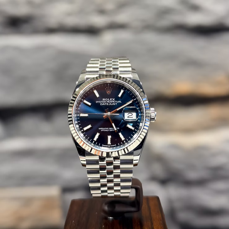 Silberne Rolex Oyster Perpetual Datejust Uhr mit blauem Zifferblatt und Datum auf einem Holzständer.