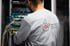 Rückenansicht eines Mannes im grauen Sweatshirt mit Firmenlogo "Hecht-Zeller AG" vor einem Serverschrank.