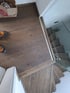 Blick auf einen dunklen Holzfußboden und eine Holztreppe mit Glasgeländer.