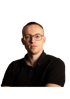 Ein junger Mann mit Brille und schwarzem Poloshirt blickt ernst direkt in die Kamera.