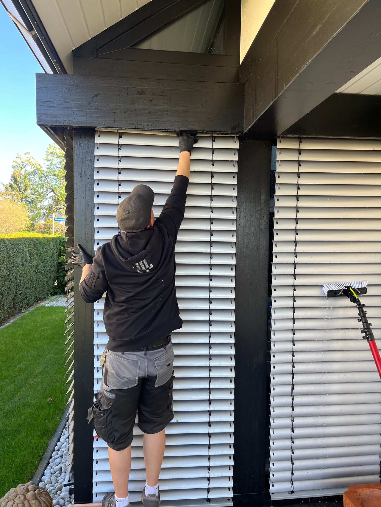 Fensterputzer in Berlin: Reinigung von Außenjalousien per Hand an einem modernen Haus.