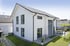 Modernes weißes Einfamilienhaus mit Satteldach, dunklen Fensterrahmen und gepflegtem Garten mit Terrasse.