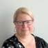 Porträt einer blonden Frau mit Brille, Creolen und gemustertem Oberteil vor hellem Hintergrund.