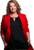 Lachende Frau mit blonden Locken, rotem Blazer, schwarzem Oberteil und Händen in den Taschen.