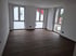Leeres Zimmer mit Holzboden und drei hohen Fenstern, die Tageslicht hereinlassen.