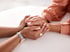 Zwei Personen halten sich an den Händen auf einem weißen Tisch, eine Person trägt eine Uhr und einen Ring.