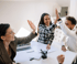 Drei Personen geben sich im Büro ein High-Five, eine Frau mit Brille lächelt.