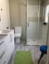 Modernes Badezimmer mit weißer Toilette, Duschkabine, Waschtisch, grauem Boden und grünem Teppich.