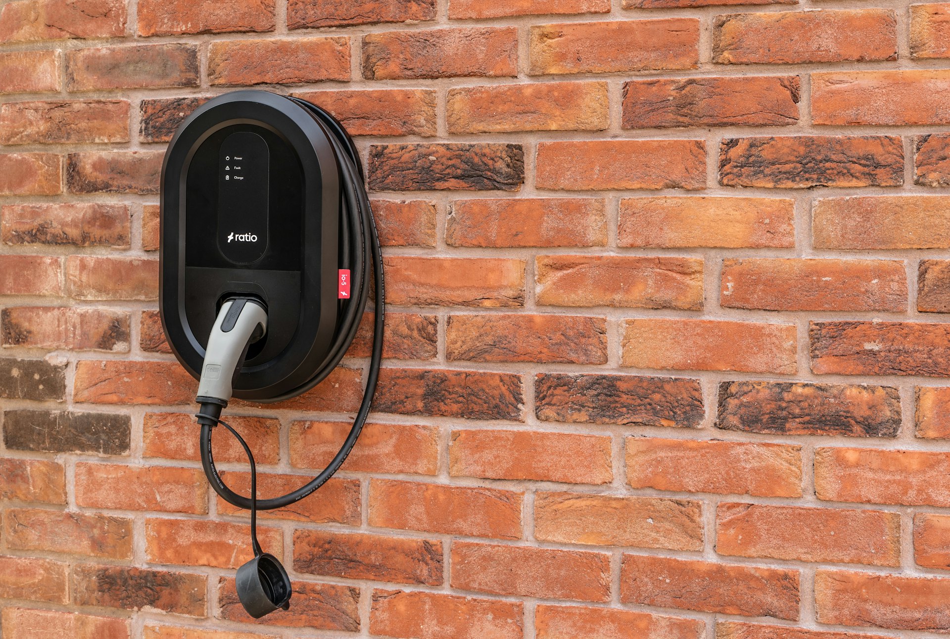 A wall-mounted Level 2 EV charger with its cable holstered on a residential garage wall