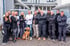 Eine Gruppe von 13 Personen und ein Hund stehen vor zwei Vans und einem Gebäude.