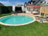 Runder Einbaupool im Garten mit angrenzender Terrasse, Gartenhaus, Pavillon und Sonnenliegen auf einer Rasenfläche.