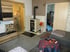 Wohnzimmer mit Kaminofen, Sideboard in Holzoptik, rundem Tisch mit gemusterter Decke und zwei Zimmertüren.