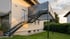 Dunkelgraue Metalltreppe führt zu einem Balkon an der Rückseite eines Hauses mit Rasen.