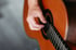 Nahaufnahme einer Hand, die die Saiten einer klassischen Akustikgitarre aus Holz zupft.