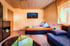 Gemütliches Wohnzimmer mit Sofa, Bett, Schrank und einem Fenster mit orangefarbenem Vorhang.