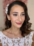 Frau mit dunklen, gewellten Haaren und weißer Blütenhaarspange, trägt ein weißes Spitzenkleid und Make-up.