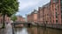 Historische Backsteingebäude der Speicherstadt in Hamburg an einem Kanal mit Brücke unter bewölktem Himmel.