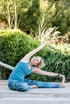 Frau macht eine seitliche Dehnung beim Yoga im Sitzen auf einer Holzterrasse im Garten.