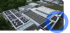 Luftbild von Fabrikdächern mit zahlreichen Solarmodulen, umgeben von Bäumen und Gebäuden.