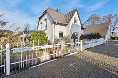 Einfamilienhaus mit weißem Zaun und gepflastertem Gehweg unter blauem Himmel.