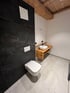 Modernes Badezimmer mit schwarzer Marmorwand, weißer Toilette, Holzwaschtisch und weißen Fliesen Reutte