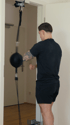 Ein Mann mit schwarzem T-Shirt und Shorts trainiert an einem hängenden Boxball in einem Türrahmen.