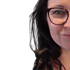 Porträt einer lächelnden Frau mit dunklen Haaren und Brille vor schwarzem Hintergrund.