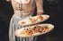 Kellnerin in Tracht serviert zwei ovale Teller mit Vorspeisen, darunter Lachs und eine Pastete.