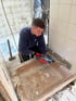 Handwerker entfernt mit einem elektrischen Meißelhammer weiße Fliesen von einer Wand im Badezimmer.