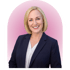 Blonde woman smiling in a navy blue blazer and white blouse against a pink background.