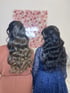 Zwei Frauen mit welligen Haaren, die von hinten vor einer beleuchteten Blumenwand stehen.