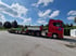 Roter Scania-Sattelzug mit beladenem Tieflader auf einem Parkplatz unter blauem Himmel.