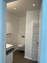 Weißes Badezimmer mit wandhängendem WC, beheiztem Handtuchhalter, Waschbecken und grauen Bodenfliesen.