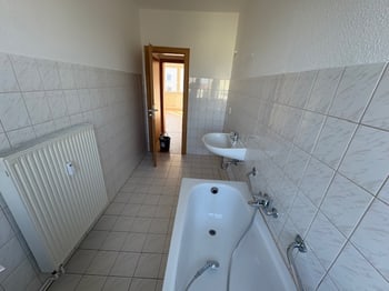 Badezimmer mit Wanne im Vordergrund, Heizkörper und Blick zum Flur