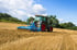 Grüner Fendt-Traktor mit blauem Grubber auf einem trockenen Feld vor einem blauen Himmel.