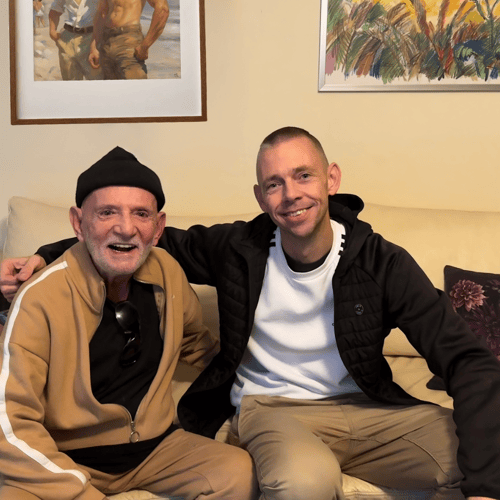 Zwei lächelnde Männer sitzen nebeneinander auf einem Sofa