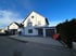Modernes weißes Einfamilienhaus mit Garage und gepflasterter Einfahrt unter blauem Himmel.