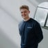 Ein lächelnder junger Mann mit blonden Haaren trägt einen dunkelblauen Pullover mit „reanmo“-Logo.