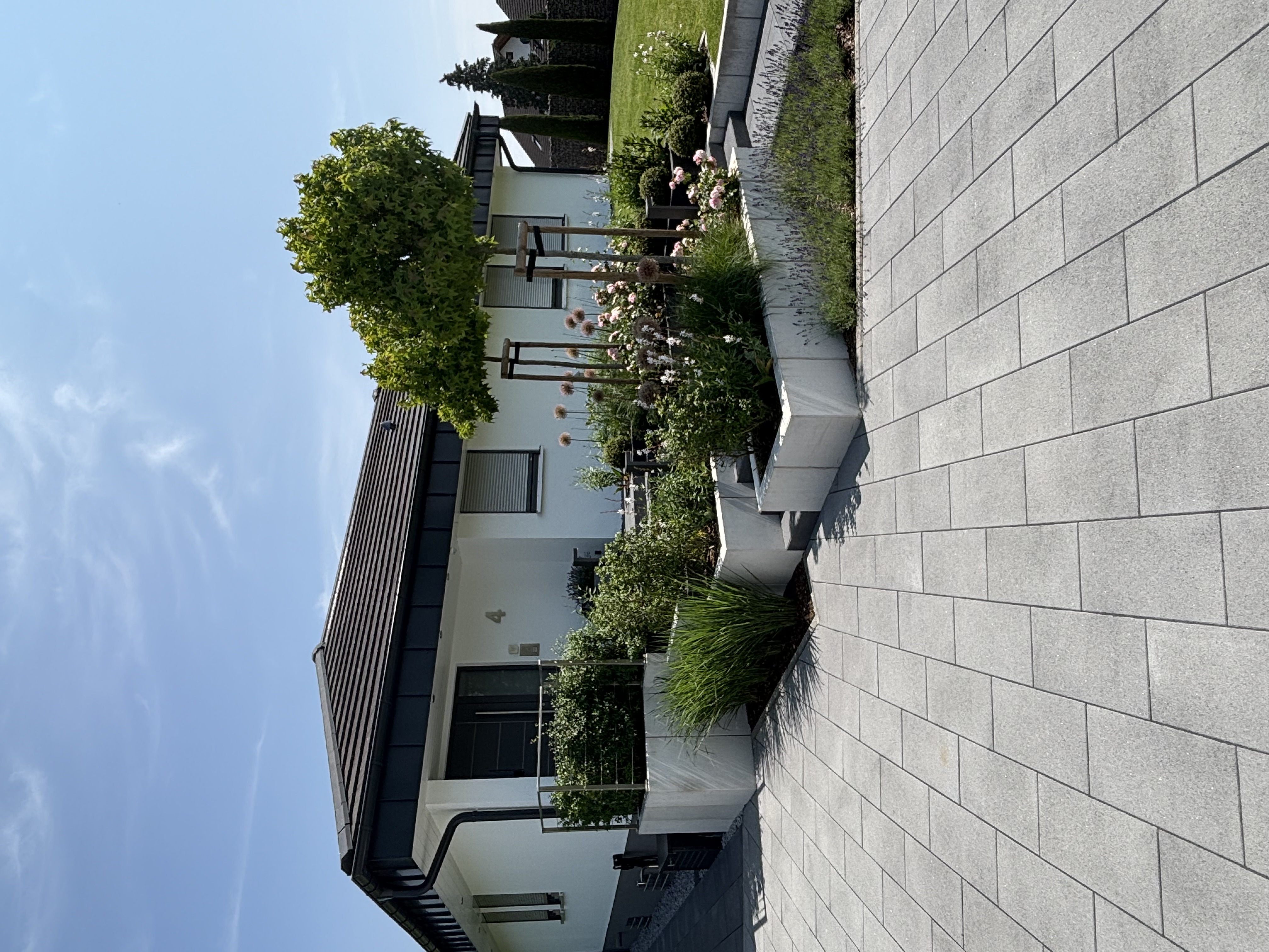 Moderne Hausfassade mit der Hausnummer 4, umgeben von gepflastertem Weg und terrassierten Beeten mit Pflanzen.