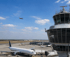 Flugzeug startet vom Flughafen, ein weiteres steht am Gate neben einem Kontrollturm unter blauem Himmel - Software-KRITIS Notfall- und Krisenmanager (NKM®).