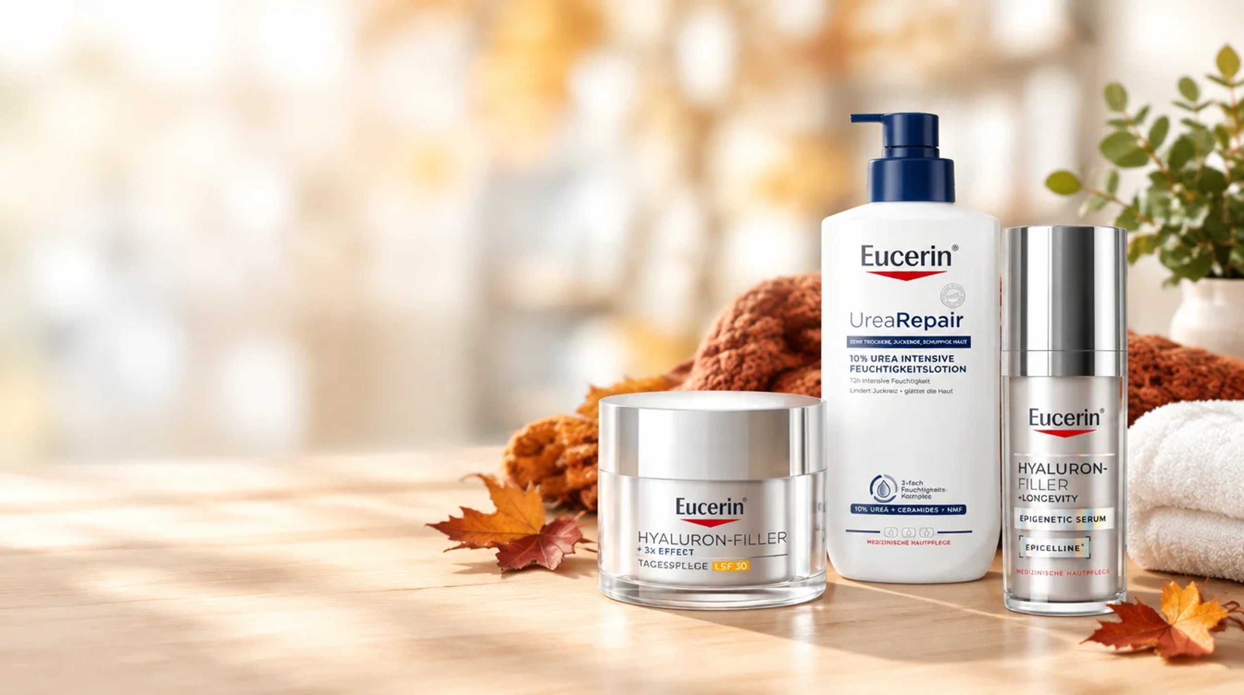 Eucerin Hyaluron-Filler Tagespflege, UreaRepair Lotion und Hyaluron-Filler Serum auf einem Holztisch mit Herbstlaub