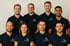 Acht Menschen in dunkelblauen Poloshirts mit dem Logo "JM Entrümpelung" stehen vor einer hellen Wand.