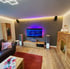 Wohnzimmer mit Fernseher, der blaue Lichtwellen zeigt, Holzböden und Ledersofa, beleuchtet mit LED-Streifen.