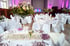 Festlich gedeckter Tisch mit lila Tellern, Besteck, Gläsern und Blumenarrangement in einem großen Raum.