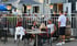 Menschen sitzen an Tischen auf einer belebten Restaurantterrasse mit Sonnenschirmen und Laternen.