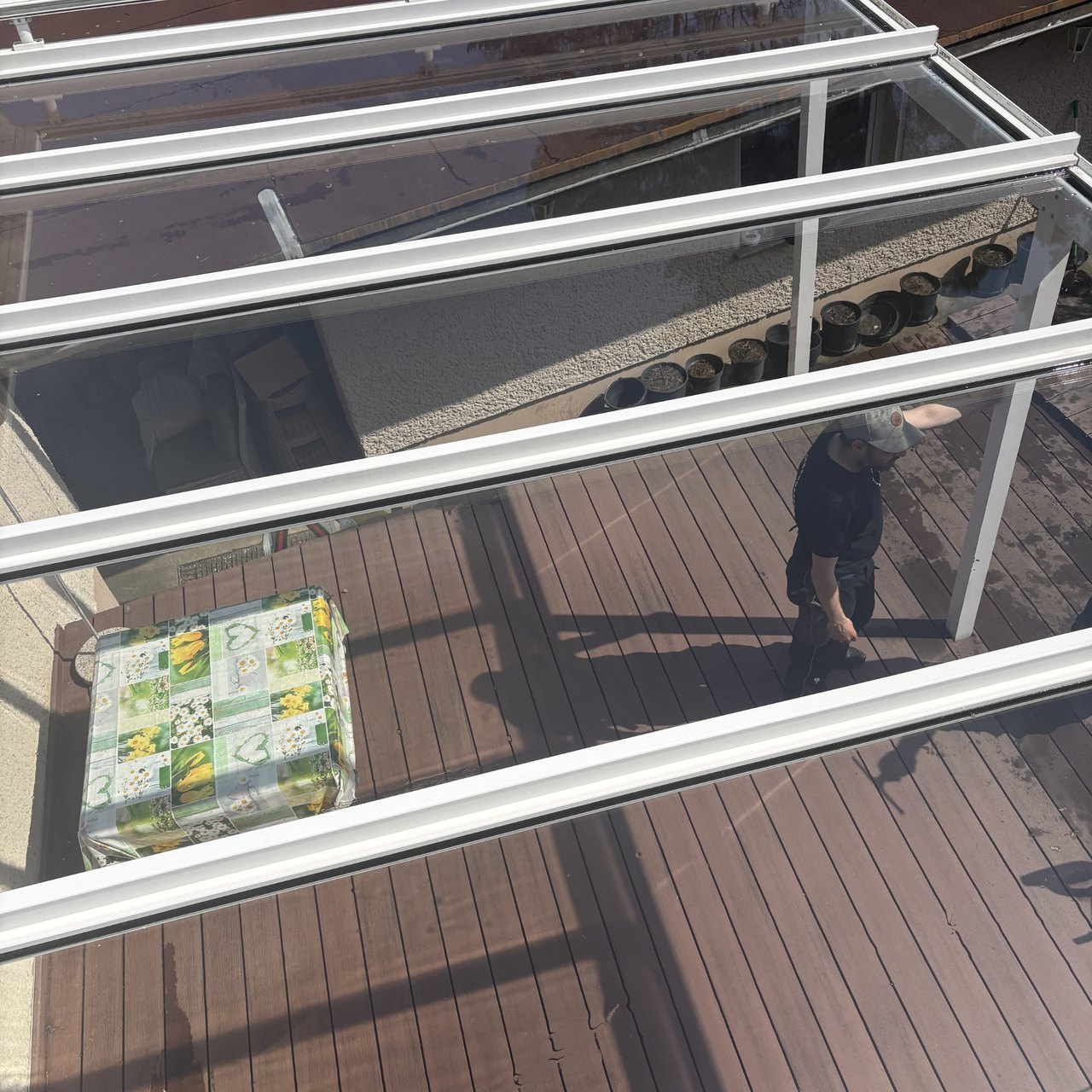 Draufsicht auf eine Terrassenüberdachung aus Glas und weißem Metallrahmen mit einem Mann und einem Tisch darunter.