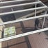 Draufsicht auf eine Terrassenüberdachung aus Glas und weißem Metallrahmen mit einem Mann und einem Tisch darunter.